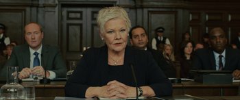Movie still from “Skyfall” (2012), directed by Sam Mendes – An older woman sitting in front of a microphone; Close Up shot, Low angle