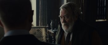 Movie still from “Skyfall” (2012), directed by Sam Mendes – An older man sitting in front of a table; Close Up shot, Over the shoulder angle