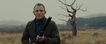 Movie still from “Skyfall” (2012), directed by Sam Mendes – A man holding a rifle in a field; Close Up shot, Over the shoulder angle