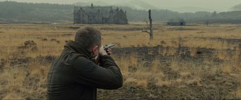 Movie still from “Skyfall” (2012), directed by Sam Mendes – A man holding a gun while standing in the middle of a field; Wide shot, Over the shoulder angle