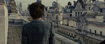 Movie still from “Skyfall” (2012), directed by Sam Mendes – A person standing on a balcony looking out at a city; Medium shot, Low angle