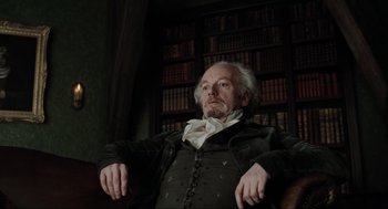 Movie still from “Sleepy Hollow” (1999), directed by Tim Burton – An older man sitting in a chair in front of a book case; Medium shot, Low angle