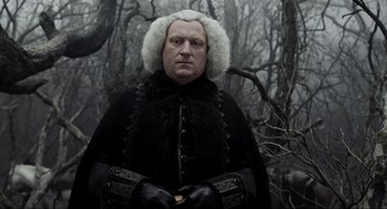 Movie still from “Sleepy Hollow” (1999), directed by Tim Burton – A man in a black coat and white wig standing in front of trees; Close Up shot, Over the shoulder angle