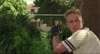 Movie still from “Bottle Rocket” (1996), directed by Wes Anderson – A young man holding a baseball bat while standing next to a tree; Close Up shot, Low angle