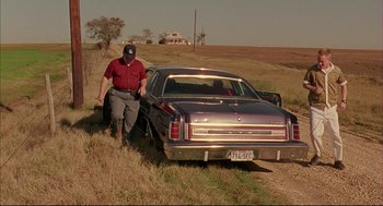 Movie still from “Bottle Rocket” (1996), directed by Wes Anderson – An older man standing next to an old car; Wide shot, High angle