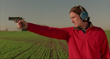 Movie still from “Bottle Rocket” (1996), directed by Wes Anderson – A man wearing headphones and a red shirt is in a green field; Medium shot, Low angle