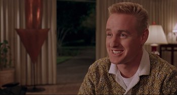 Movie still from “Bottle Rocket” (1996), directed by Wes Anderson – A young man smiles while sitting in front of a window; Close Up shot, Low angle