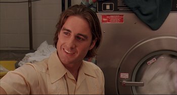 Movie still from “Bottle Rocket” (1996), directed by Wes Anderson – A man in a tan shirt smiling in front of a washing machine; Close Up shot, Low angle