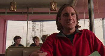 Movie still from “Bottle Rocket” (1996), directed by Wes Anderson – A man in a red jacket sitting in front of two other men; Close Up shot, Over the shoulder angle