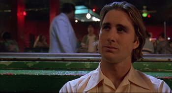 Movie still from “Bottle Rocket” (1996), directed by Wes Anderson – A person sitting in a room; Close Up shot, Low angle
