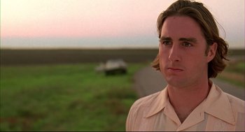 Movie still from “Bottle Rocket” (1996), directed by Wes Anderson – A man standing in front of an empty road; Close Up shot, Low angle