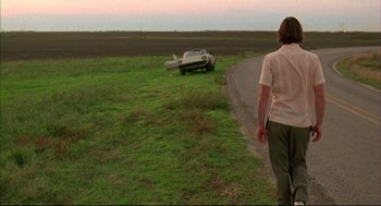 Movie still from “Bottle Rocket” (1996), directed by Wes Anderson – A man walking down a road next to an overturned car; Wide shot, Over the shoulder angle
