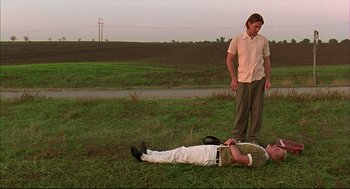 Movie still from “Bottle Rocket” (1996), directed by Wes Anderson – A man laying on the ground next to another man in a field; Wide shot, Low angle