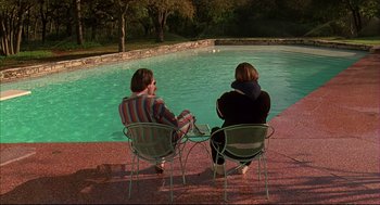 Movie still from “Bottle Rocket” (1996), directed by Wes Anderson – Two people sitting in front of a swimming pool; Wide shot, High angle