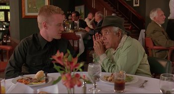 Movie still from “Bottle Rocket” (1996), directed by Wes Anderson – Two men sitting at a table in front of plates of food; Medium shot, Over the shoulder angle
