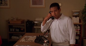 Movie still from “Bottle Rocket” (1996), directed by Wes Anderson – A man talking on a phone while standing at a table; Medium shot, Low angle
