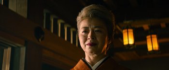 Movie still from “Snake Eyes” (2021), directed by Robert Schwentke – An older asian woman wearing an orange robe; Close Up shot, Low angle