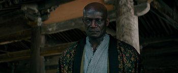 Movie still from “Snake Eyes” (2021), directed by Robert Schwentke – A man in a kimono is standing in front of a wooden structure; Close Up shot, Low angle