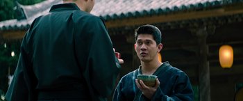 Movie still from “Snake Eyes” (2021), directed by Robert Schwentke – A man holding a bowl while standing next to another man; Medium shot, Over the shoulder angle