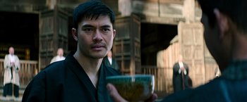 Movie still from “Snake Eyes” (2021), directed by Robert Schwentke – A man holding a bowl while wearing a black robe; Close Up shot, Over the shoulder angle