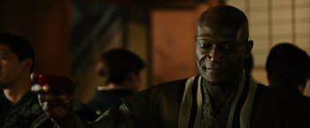 Movie still from “Snake Eyes” (2021), directed by Robert Schwentke – An older man is smiling while holding a coffee mug; Close Up shot, Over the shoulder angle