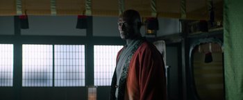 Movie still from “Snake Eyes” (2021), directed by Robert Schwentke – An older man wearing a red robe in front of a window; Medium shot, Low angle