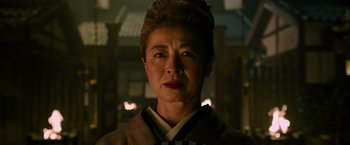Movie still from “Snake Eyes” (2021), directed by Robert Schwentke – An older asian woman wearing a suit and tie; Close Up shot, Low angle