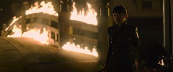 Movie still from “Snake Eyes” (2021), directed by Robert Schwentke – A woman standing in front of a burning building holding an umbrella; Medium shot, Over the shoulder angle