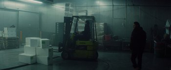 Movie still from “Snakehead” (2021), directed by Evan Jackson Leong – A man sitting in a fork lift in a warehouse; Wide shot, Low angle