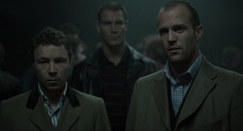 Movie still from “Snatch” (2000), directed by Guy Ritchie – A group of men standing next to each other in a room; Medium shot, Low angle