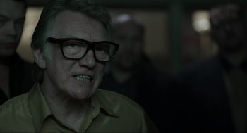 Movie still from “Snatch” (2000), directed by Guy Ritchie – An older man wearing glasses looking at the camera; Close Up shot, Over the shoulder angle