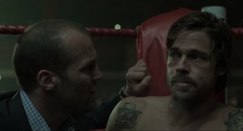 Movie still from “Snatch” (2000), directed by Guy Ritchie – A man sitting next to another man in a red chair; Close Up shot, Over the shoulder angle