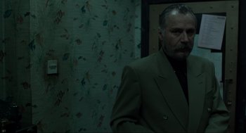 Movie still from “Snatch” (2000), directed by Guy Ritchie – A man in a suit standing in front of a wall; Medium shot, Low angle