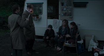 Movie still from “Snatch” (2000), directed by Guy Ritchie – A group of people sitting in front of a camper van; Medium shot, Over the shoulder angle