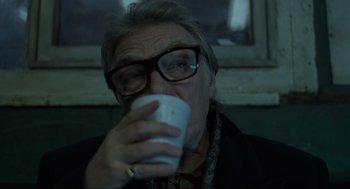 Movie still from “Snatch” (2000), directed by Guy Ritchie – An older man drinking from a white coffee cup; Close Up shot, Over the shoulder angle