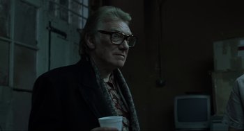 Movie still from “Snatch” (2000), directed by Guy Ritchie – An older man wearing glasses holding a cup; Close Up shot, Low angle