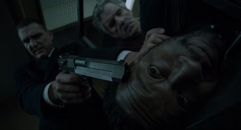 Movie still from “Snatch” (2000), directed by Guy Ritchie – A man is holding a gun while another man watches; Close Up shot, Overhead angle
