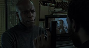 Movie still from “Snatch” (2000), directed by Guy Ritchie – A man sitting in front of a tv holding a cell phone; Close Up shot, Over the shoulder angle