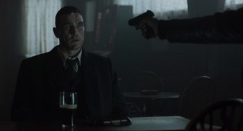 Movie still from “Snatch” (2000), directed by Guy Ritchie – A man sitting at a table with a gun pointed at him; Medium shot, Over the shoulder angle