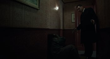 Movie still from “Snatch” (2000), directed by Guy Ritchie – A man holding a gun standing in front of a chair; Wide shot, High angle