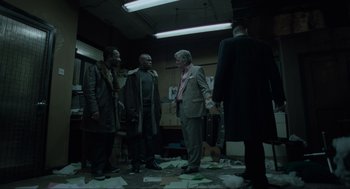 Movie still from “Snatch” (2000), directed by Guy Ritchie – A group of men standing in a room with papers on the floor; Wide shot, High angle