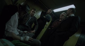 Movie still from “Snatch” (2000), directed by Guy Ritchie – A group of men sitting in a dark room next to each other; Medium shot, Low angle