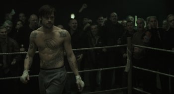 Movie still from “Snatch” (2000), directed by Guy Ritchie – A group of people in a boxing ring watching a man; Medium shot, Over the shoulder angle