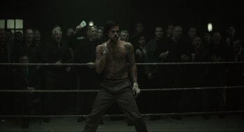 Movie still from “Snatch” (2000), directed by Guy Ritchie – A man standing in front of a crowd in a boxing ring; Wide shot, Over the shoulder angle
