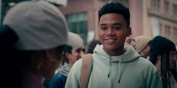 Movie still from “Sneakerella” (2022), directed by Elizabeth Allen Rosenbaum – A young man smiling while standing next to a crowd; Close Up shot, Over the shoulder angle