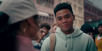 Movie still from “Sneakerella” (2022), directed by Elizabeth Allen Rosenbaum – A young man with a backpack standing in front of a group of people; Close Up shot, Over the shoulder angle