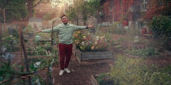 Movie still from “Sneakerella” (2022), directed by Elizabeth Allen Rosenbaum – A man standing next to a flower garden; Wide shot, Low angle