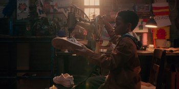Movie still from “Sneakerella” (2022), directed by Elizabeth Allen Rosenbaum – A young boy in a workshop sewing a pair of shoes; Medium shot, Low angle
