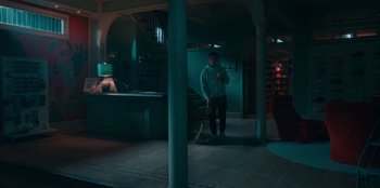 Movie still from “Sneakerella” (2022), directed by Elizabeth Allen Rosenbaum – A man holding a baseball bat while standing in a room; Wide shot, High angle