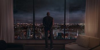 Movie still from “Sneakerella” (2022), directed by Elizabeth Allen Rosenbaum – A man standing in front of a window looking out at a city at night; Extreme Wide shot, Low angle